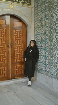 A smiling woman in black clothes poses in front of an intricate door within topkapi palace, istanbul,