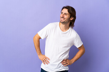 Young handsome man isolated on purple background posing with arms at hip and smiling