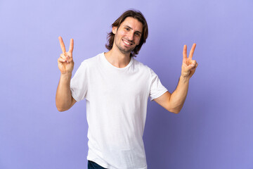Naklejka premium Young handsome man isolated on purple background showing victory sign with both hands