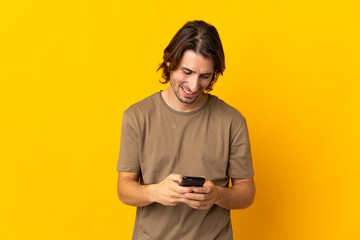 Young handsome man isolated on yellow background sending a message with the mobile