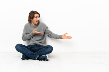 Young handsome man sitting on the floor over isolated background with surprise expression while looking side