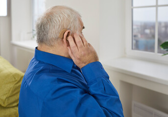 Close up portrait of a mature gray-haired senior man wearing blue shirt using his modern hearing...