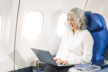 An adult woman sits by the window on a passenger plane, eagerly traveling abroad. She gazes at the...