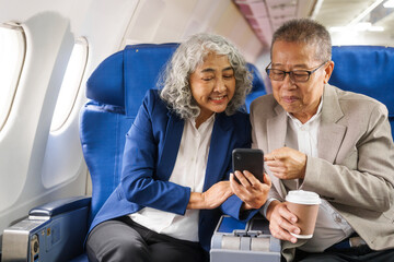 A mature couple enjoys a plane ride, seated near the window. They gaze out at the sky, savoring the view and the excitement of travel, creating cherished memories together.