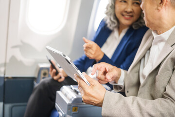 A mature couple enjoys a plane ride, seated near the window. They gaze out at the sky, savoring the view and the excitement of travel, creating cherished memories together.