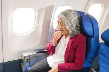 A mature woman sits by the window on a passenger plane, traveling abroad. She looks unwell, experiencing a headache, nausea, and vomiting, which dampens her travel excitement.