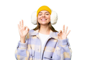 Young blonde woman wearing winter muffs over isolated chroma key background in zen pose