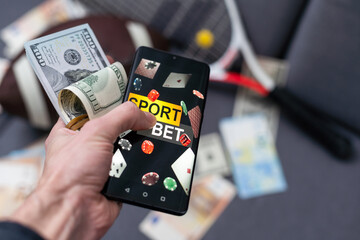 Online sports betting. Dollars are falling on the background of a hand with a smartphone and a soccer ball. Creative background, gambling