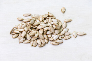 Heap of dried pumpkin seeds on a light white wooden table background.