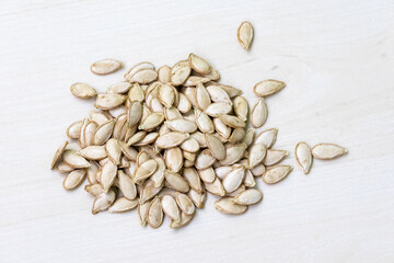 Dried pumpkin seeds on a light white wooden surface.