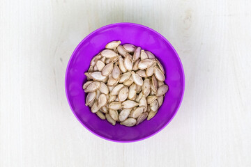 Dried pumpkin seeds on a plastic bowl on wooden background.