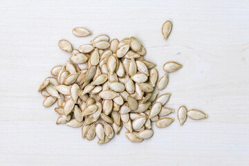 Dried pumpkin seeds on a light white wooden surface. Top view.