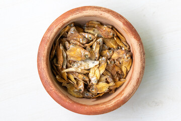 Dried rupchanda shutki or chinese pomfret fish in earthen pot on light white wooden background. Top view.