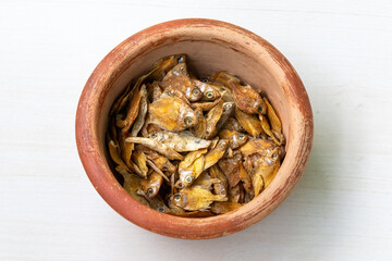 Dried rupchanda shutki or chinese pomfret fish in earthen pot on light white wooden background.