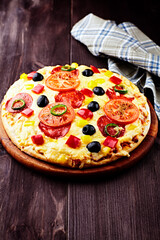 Pizza with salami, black olives, tomatoes and red, yellow and jalapeno pepper. Dark wooden background. Copy space.	
