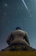 A statue of Buddha below a starlit sky with a falling star.