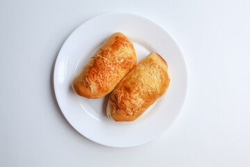 Two baked bread with grated cheese on top, on white plate, isolated on white background, flat lay or top view