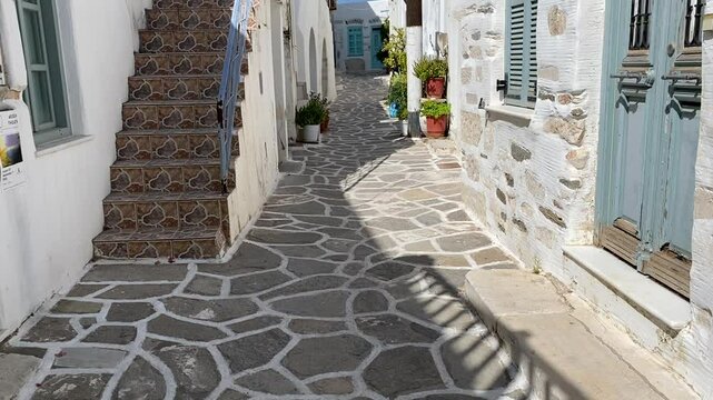 Beautiful cobbled street with white buildings and pink flowers growing from a tree. Paros Greece 4K footage