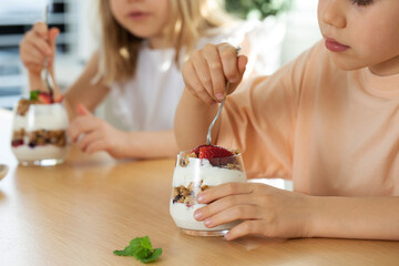 Children enjoy a healthy breakfast of granola with yogurt, decorated with fresh berries,