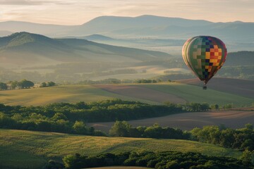 Fototapeta premium A hot air balloon drifting above rolling hills, with a softly blurred background of green fields and distant mountains. 