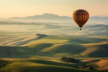 Obraz premium A hot air balloon drifting above rolling hills, with a softly blurred background of green fields and distant mountains. 