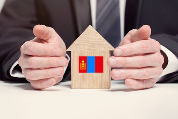 Businessman hand holding wooden home model with Mongolian flag. insurance and property concepts