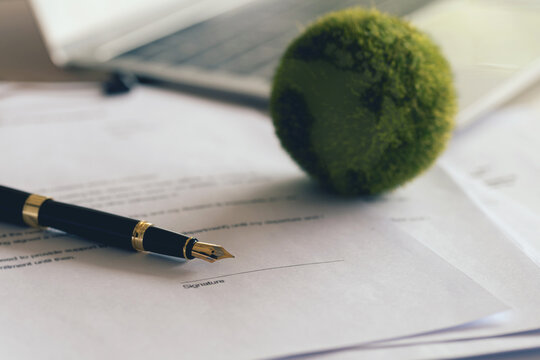 ink pen with papers and a green world on the desk. the idea for managing business document agreements and approving Green business companies with eco-friendly waste management regulation concepts.ESG.