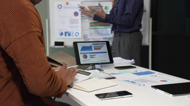 A collaborative meeting at an office desk focusing on teamwork, with discussions centered around financial charts and the sub-account management of work in process in production cost accounting.