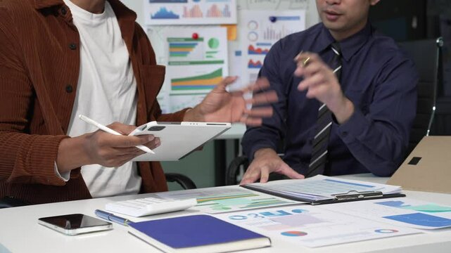 A collaborative meeting at an office desk focusing on teamwork, with discussions centered around financial charts and the sub-account management of work in process in production cost accounting.