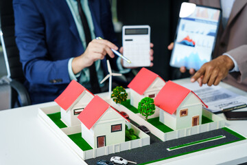 A meeting at an office desk focuses on teamwork with a house model and discussions on electric...