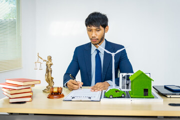 A male Asian lawyer in a formal suit works at his desk, focusing on contracts and legal matters,...