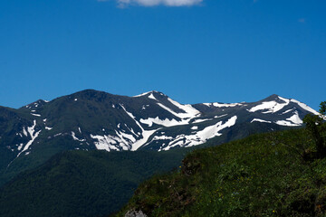 Snow-capped mountains and green hills under blue sky.