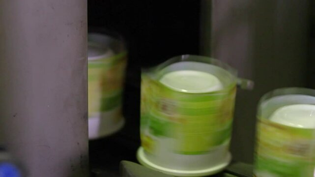 Label application process, close-up. Machine for sticker on product in manufacture. Flexible packaging. Industrial application of labels to food containers at a plastic packaging factory