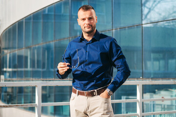 Man in Blue Shirt Holding Glasses on a Modern Building Balcony