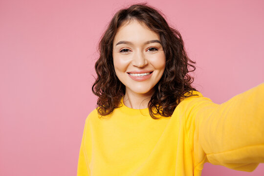 Close up young smiling happy woman she wearing yellow sweatshirt casual clothes doing selfie shot pov on mobile cell phone isolated on pastel light pink background studio portrait. Lifestyle concept.