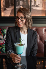 Young attractive woman sitting in a bar and drinking cocktails after work. Business casual dress code in a cafe. Young woman smiling and drinking.