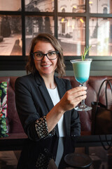 Young attractive woman sitting in a bar and drinking cocktails after work. Business casual dress code in a cafe. Young woman smiling and drinking.
