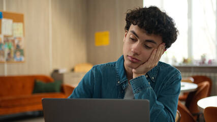 Caucasian tired bored sad upset fatigued man male student guy boy schoolboy pupil internet lesson school university campus cafe studying learning boring problem education laptop computer e-learning