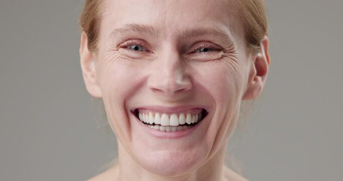 Real people - concept of age, beauty, health and dry skin care - beautiful mature Caucasian middle-aged woman in her 50s looks with a calm confident look at the camera, smiles a bright toothy smile
