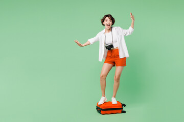 Full body surprised traveler woman wear casual clothes stand on suitcase bag pov ride skate or fly isolated on plain green background. Tourist travel abroad in free time rest. Air flight trip concept. © ViDi Studio