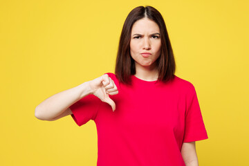 Young sad dissatisfied disappointed woman wear pink t-shirt casual clothes showing thumb down dislike gesture look camera isolated on plain yellow orange background studio portrait. Lifestyle concept.