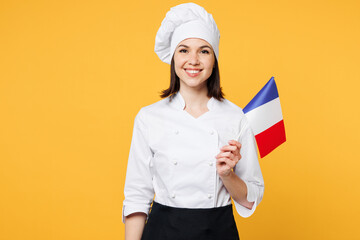 Young smiling happy chef cook baker woman wears white shirt black apron uniform toque chefs hat hold in hand French flag looking camera isolated on plain yellow background studio Cooking food concept