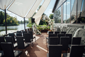 Modern area for an outdoor ceremony. Round arch with dark chairs for guests and a sun canopy