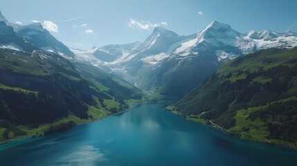 Stunning aerial view of snow-capped mountains and a serene blue lake surrounded by green valleys under a clear sky.
