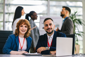 Two business people working together on laptops and tablets in office.