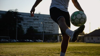 Legs of young man kicking ball at green field. Male feet of professional footballer juggling soccer...