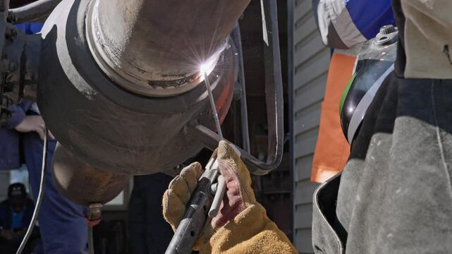 A welder engaged in industrial metalwork focuses on joining large pipes with a high-intensity welding torch, showcasing precision and skill critical to metal fabrication and construction.
