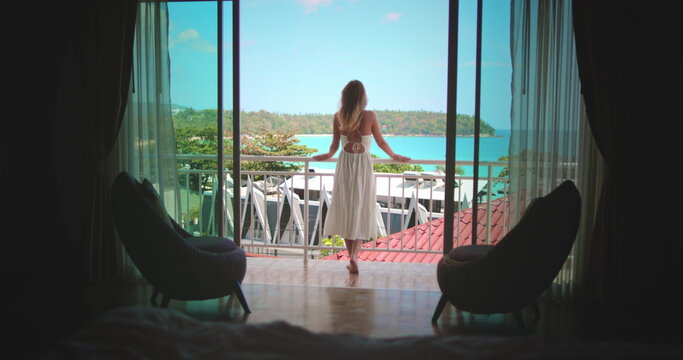 Beautiful caucasian woman on balcony, enjoy ocean view from hotel room apartment, sunny day. Outdoor lifestyle travel summer holiday vacation. Phuket tropical island, Thailand. Back view