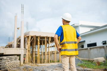 Fototapeta premium An architect, wearing a hardhat and safety vest, checks a laptop and house plan paper on a clipboard. Blueprints and construction documents lie nearby, emphasizing safety and precision in building.