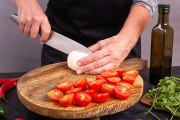 View of the process of preparing fresh vegetable salad with mozzarella cheese on a wooden chopping board, closeup with selective focus